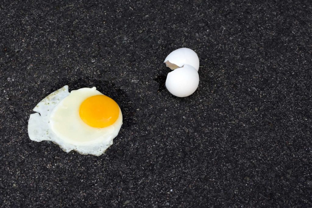 Fried egg and a cracked eggshell on the sidewalk