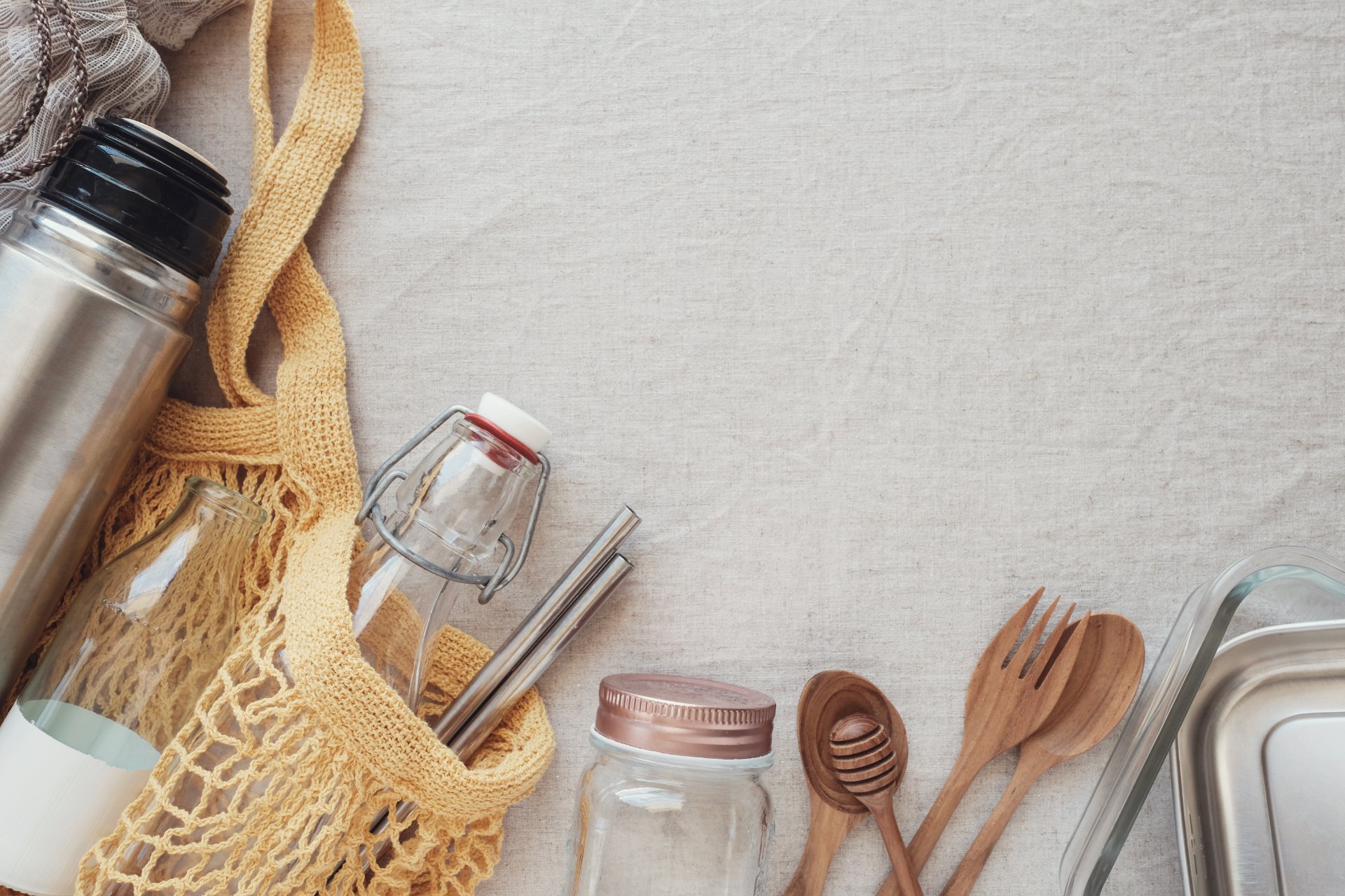 An assortment of green living items, including a reusable coffee mug, a reusable water bottle, metal straws, a glass jar, wooden utensils and baking ware.