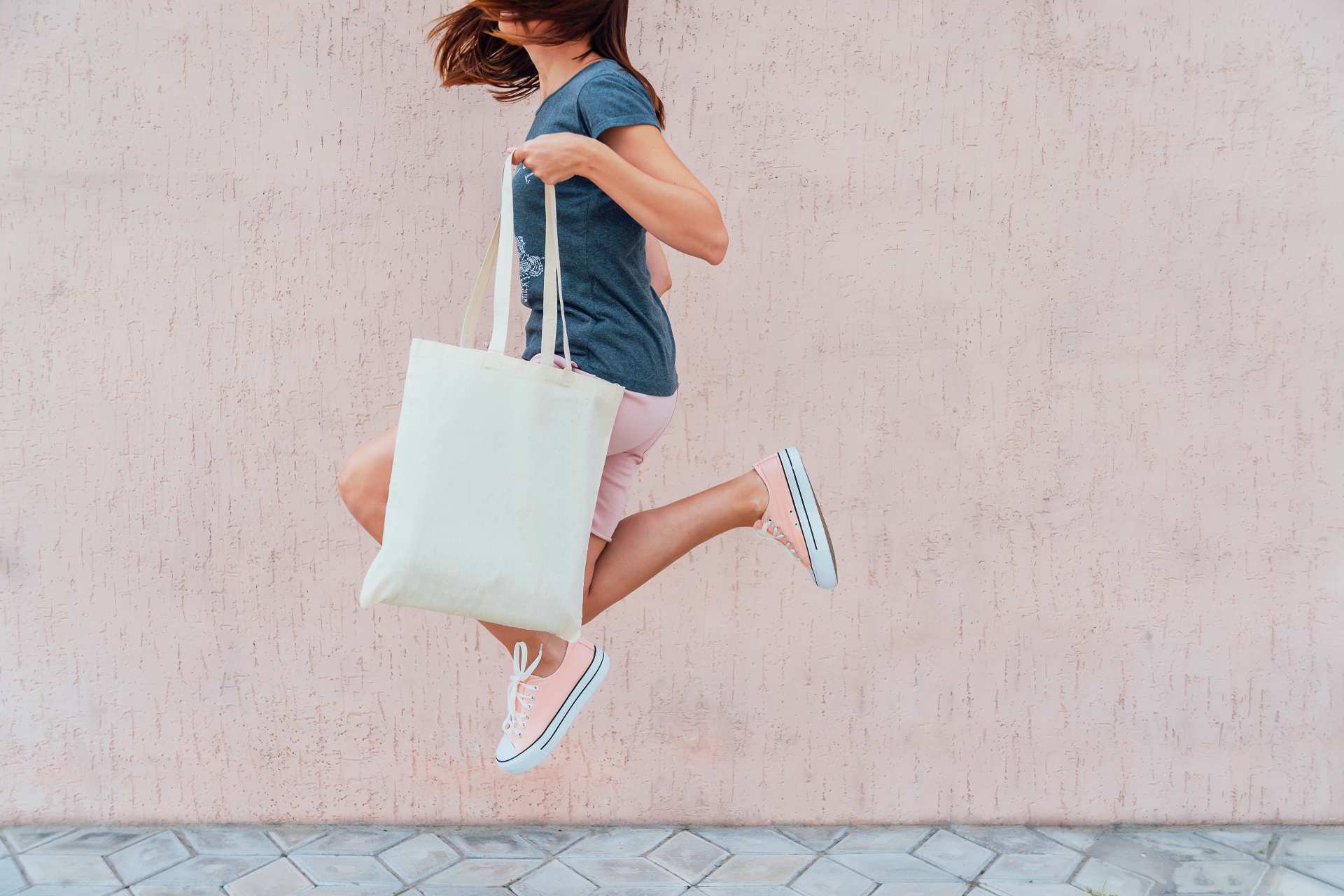 A woman jumping while holding a reusable canvas tote