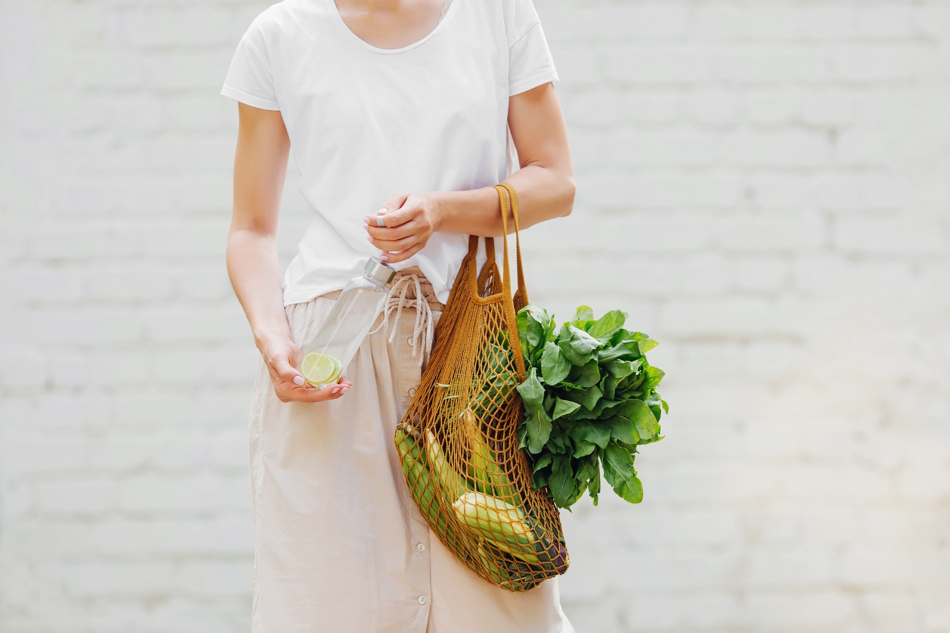 Female hands hold eco bag of vegetables, greens and reusable water bottle.