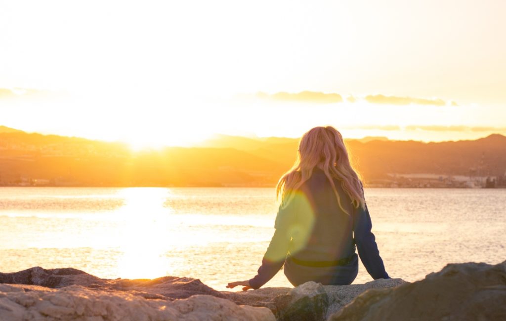 A woman looking out onto a sea with a sunset on the horizon